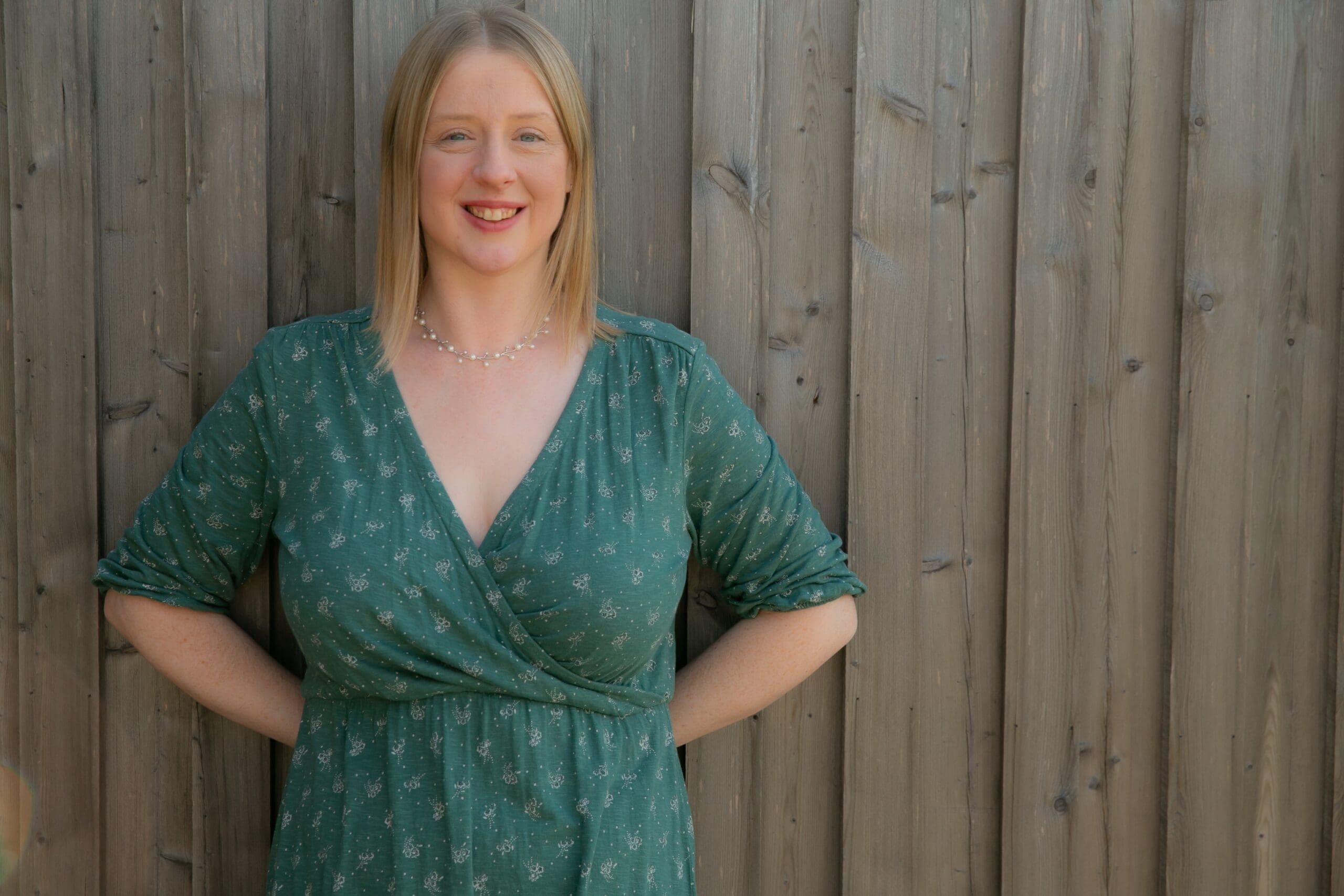 Photo of Emily Hill in a green dress standing in front of a fence.